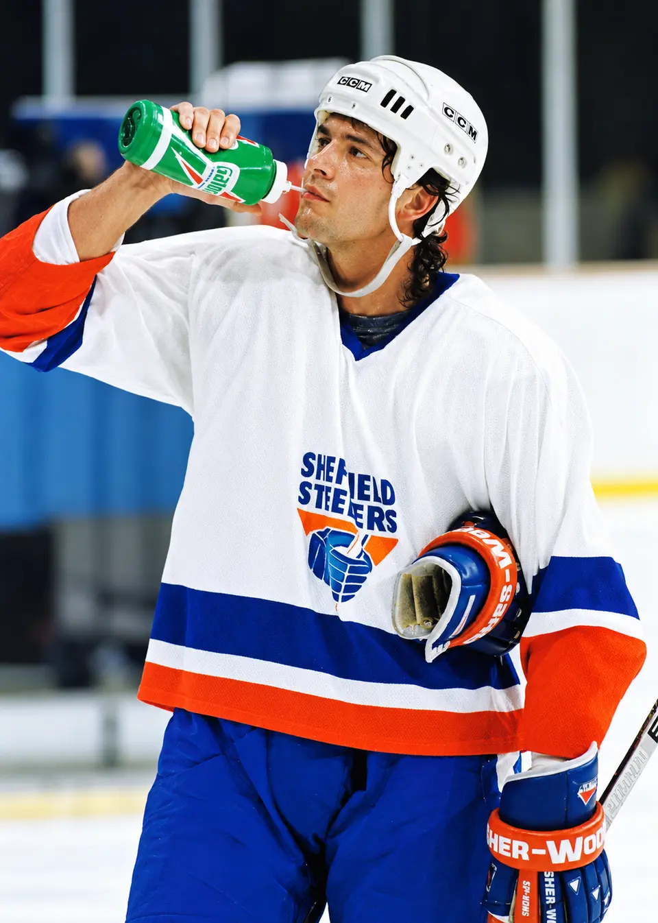 Rocket Ron Shudra, one of the defining figures in Sheffield Steelers history. Rocket Ron Shudra wearing a white Sheffield Steelers jersey and helmet while drinking from a water bottle beside the ice.
