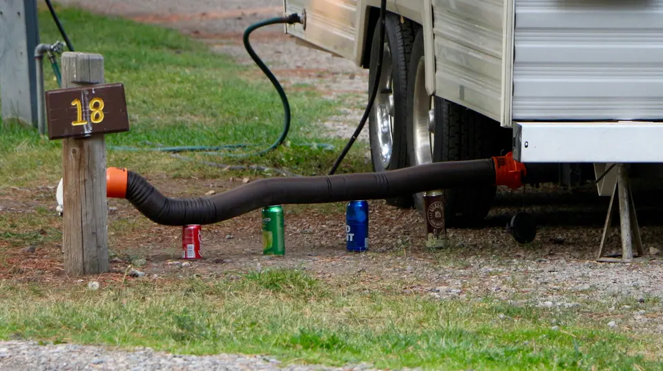 An RV black tank is connected for dumping with the slinky hose at site 18. The hose is held up with different height soda cans.
